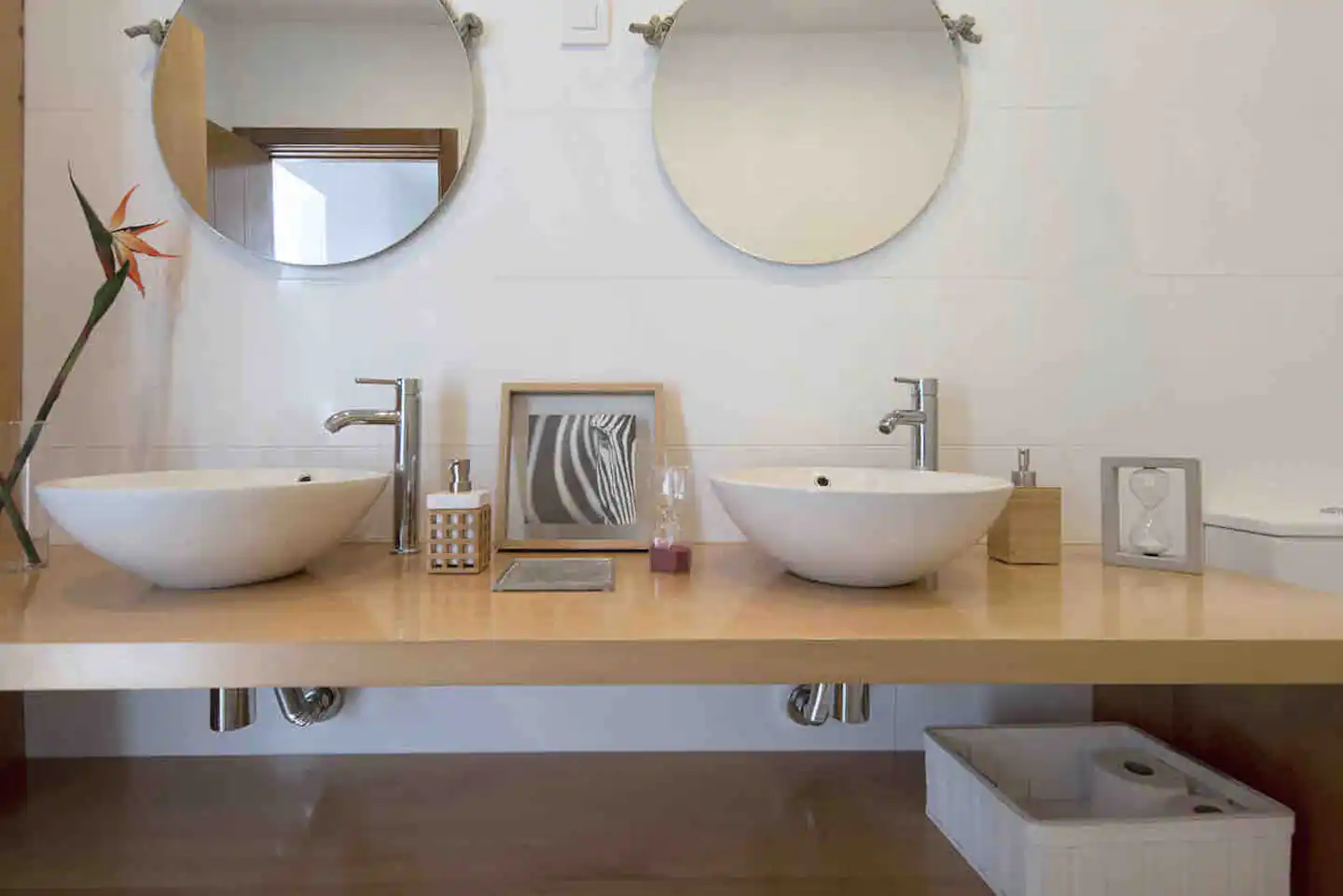 Baño con doble lavabo sobre encimera de madera y dos espejos redondos