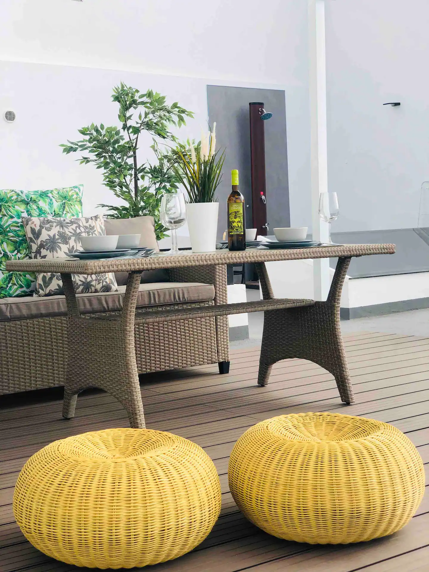 Mesa exterior de ratán puesta, con pufs amarillos sobre la tarima de madera