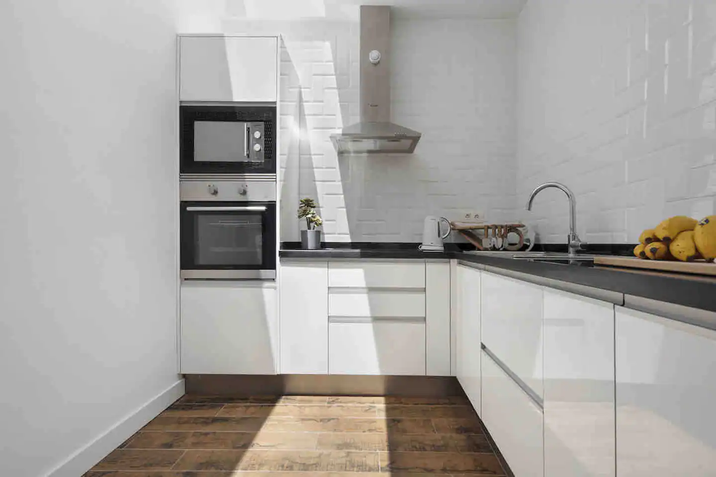 Cocina blanca con horno y microondas empotrados, campana extractora y suelo de madera