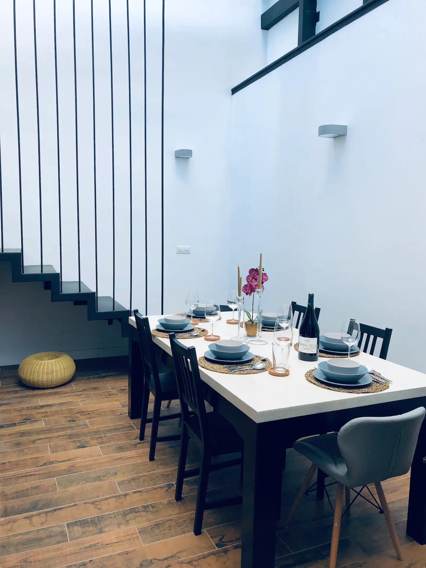 Comedor con mesa blanca puesta para seis, bajo la escalera de la casa