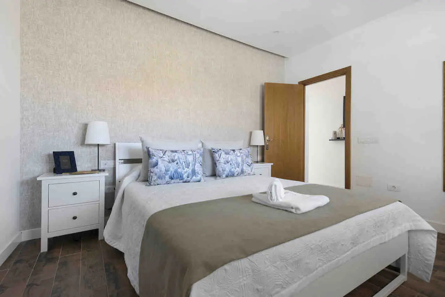 Segundo dormitorio en tonos claros, con cama de matrimonio y mesillas blancas