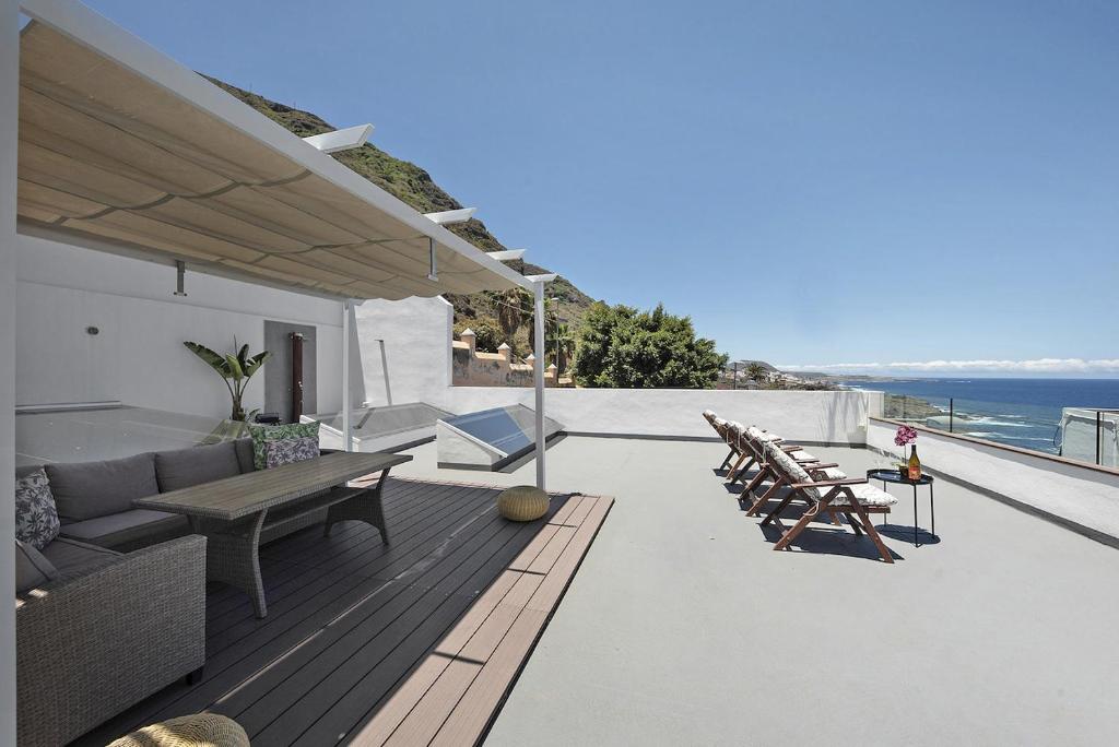 La azotea de 110 m² de Bella Home: pérgola con sofá, tumbonas alineadas y el Atlántico al fondo tras la barandilla